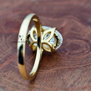 May include: A gold ring with a large, oval-shaped clear gemstone. The gemstone is surrounded by smaller, clear stones and set in a decorative gold setting. The ring band is also gold.