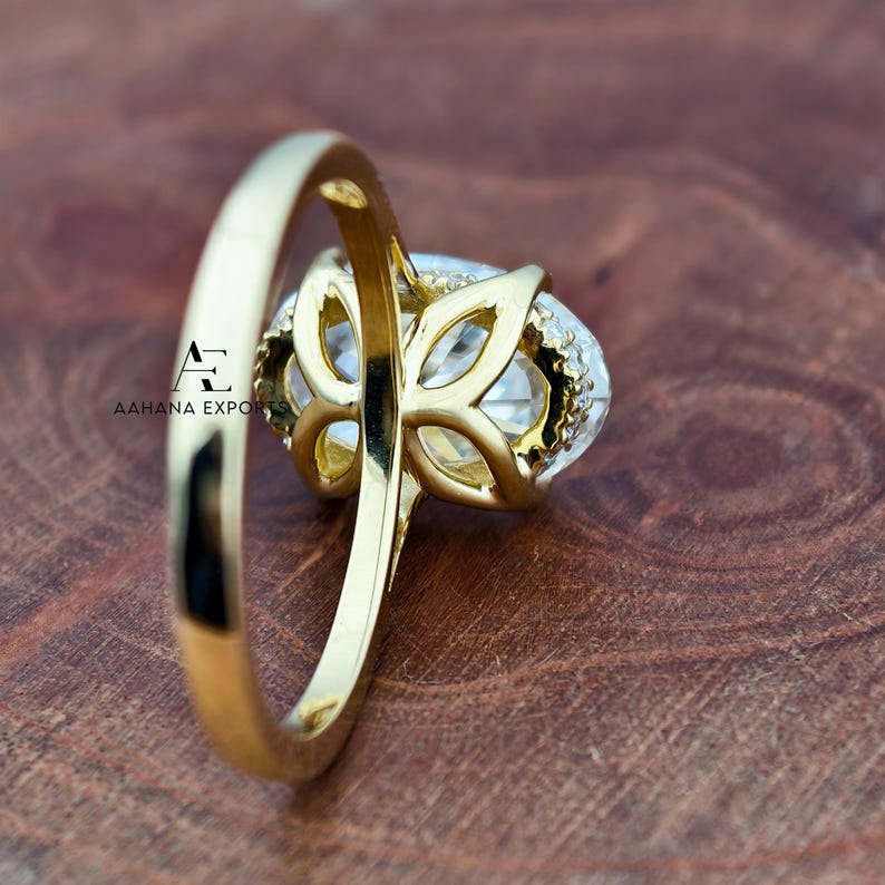 May include: A gold ring with a large, oval-shaped clear gemstone. The gemstone is surrounded by smaller, clear stones and set in a decorative gold setting. The ring band is also gold.