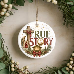 Puede incluir: Un adorno redondo de cer&aacute;mica blanca con el texto TRUE STORY en letras verdes y rojas. El dise&ntilde;o incluye una cruz de madera, una escena de nacimiento con figuras, un pesebre, pinos y un lazo rojo, todo acentuado por una estrella dorada.
