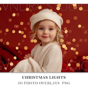May include: A young girl wearing a white knit hat sits in front of a red background with gold bokeh lights. The girl is wearing a white sweater and has blonde hair.