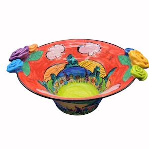 Puede incluir: Un cuenco de cerámica pintado a mano con un diseño de paisaje vibrante. El cuenco presenta un exterior rojo con una escena pintada de colinas, nubes y flores. Rosas esculpidas de colores adornan el borde. El interior es de color verde brillante.
