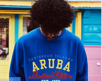 May include: Blue sweatshirt with "ARUBA Limited Edition" text in yellow and red. The text "Caribbean Islands" is above the word "ARUBA". The sweatshirt has the Aruba flag on the left side. The text "EST. 1986" is below the text "Limited Edition".