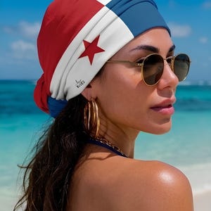 May include: A turban with a red, white, and blue design, featuring a red star. The turban is worn by a person wearing gold-rimmed sunglasses and gold hoop earrings. The background shows a beach and ocean.