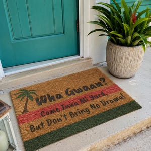 May include: A rectangular doormat with the text "Wha Gwaan? Come Inna Mi Yard, But Don't Bring No Drama!" features a palm tree graphic. The mat has brown, red, and green stripes and is placed in front of a teal door.