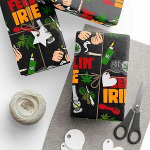 May include: Black wrapping paper with a cannabis-themed design featuring marijuana leaves, lighters, and the words "Feel Irie" and "Rollin' E". The wrapped gifts are tied with twine and adorned with star and heart-shaped tags. A ball of twine and scissors are also present.