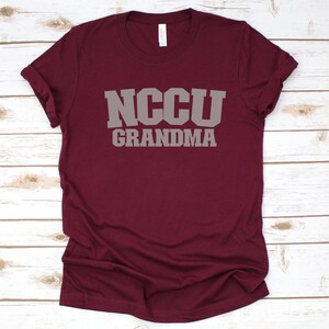 K&ouml;nnte beinhalten: Burgunderfarbenes T-Shirt mit dem Text "NCCU GRANDMA" in grauer Schrift.