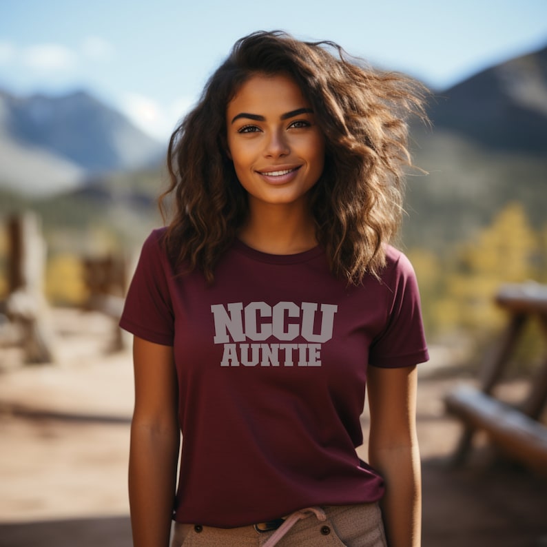 K&ouml;nnte beinhalten: Ein maroonfarbenes T-Shirt mit dem Aufdruck "NCCU AUNTIE" in Wei&szlig; auf der Vorderseite.