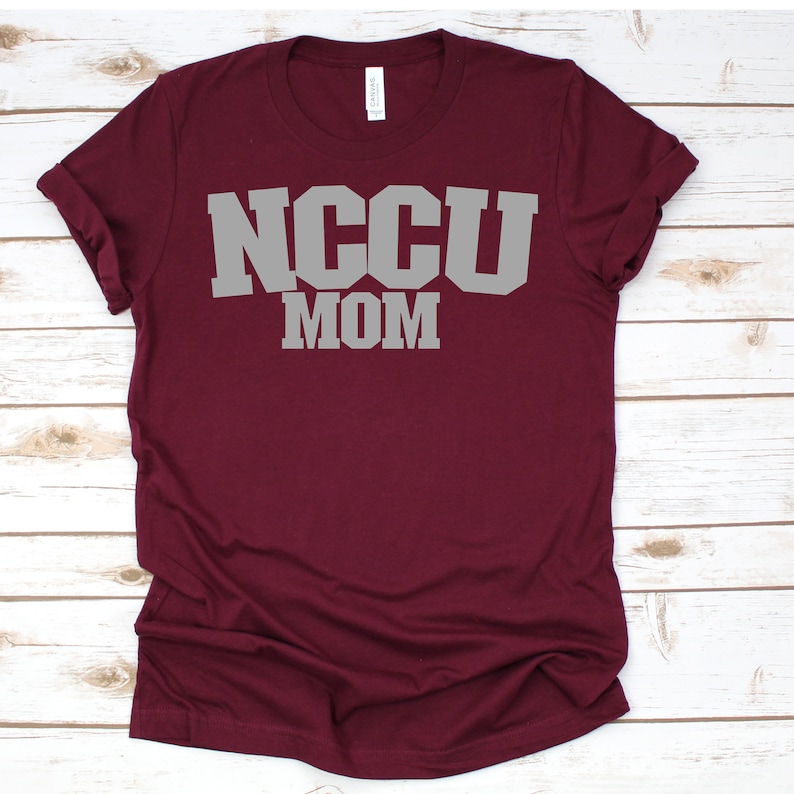 K&ouml;nnte beinhalten: Burgunderfarbenes T-Shirt mit dem Text "NCCU MOM" in grauen Buchstaben.