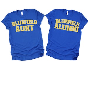 Puede incluir: Dos camisetas azul real con mangas enrolladas. Una camiseta tiene el texto "BLUEFIELD AUNT" en letras amarillas. La otra camiseta tiene el texto "BLUEFIELD ALUMNI" en letras amarillas.