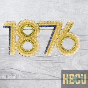 May include: A gold-toned brooch in the shape of the number "1876". The brooch is embellished with small, round, white and yellow gems, and blue gems. The brooch has a pin on the back. The letters "HBCU" are in the bottom right corner.