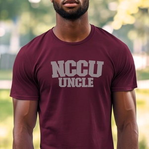 K&ouml;nnte beinhalten: Burgunderfarbenes T-Shirt mit dem Text "NCCU UNCLE" in wei&szlig;en Buchstaben.
