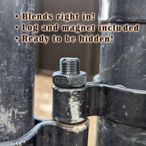 May include: A black metal geocache container with the text "GEOCACHE" printed on it. The container is attached to a black metal fence post.