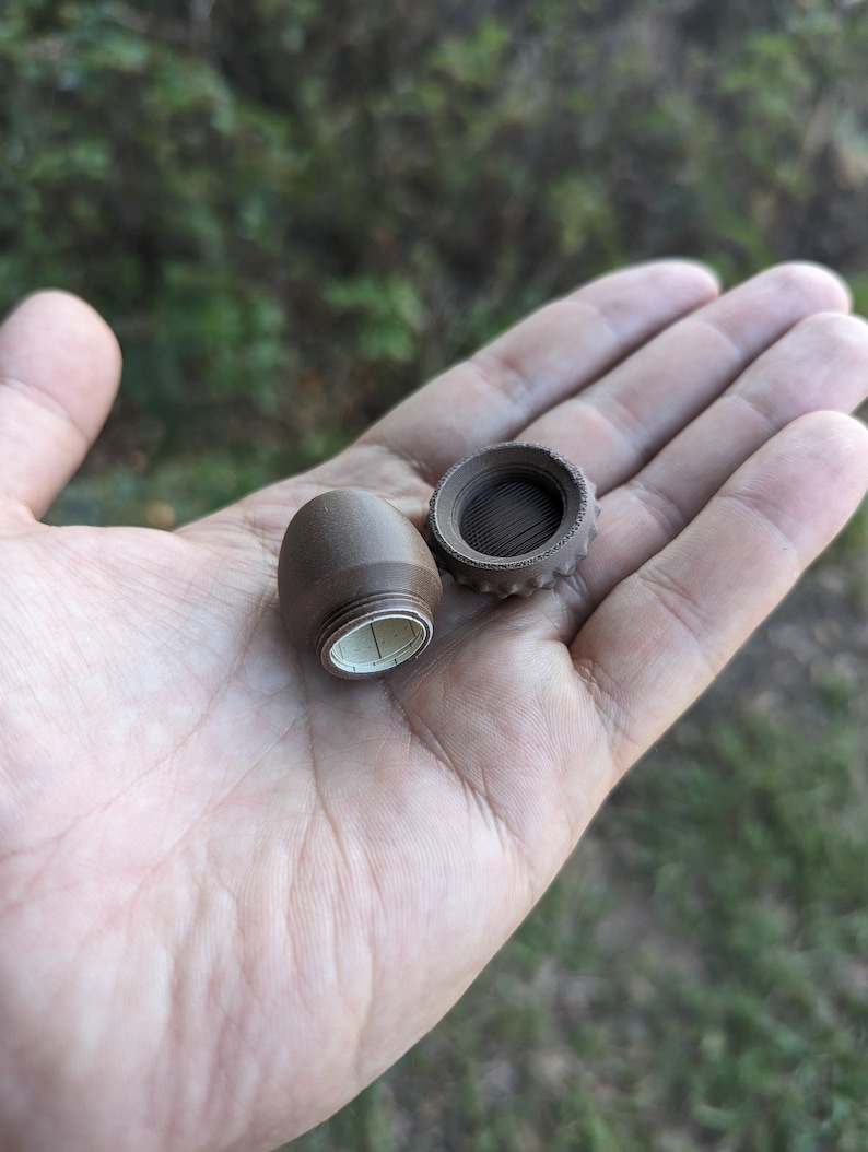 May include: Two brown, plastic, cylindrical containers with lids. One container is open and the other is closed. The open container has a white, paper label with black markings.
