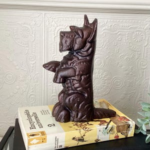 May include: A brown cast iron dog bookend. The dog is a Scottish Terrier, standing upright with its front paws extended. The bookend is resting on a vintage book with the title "Encyclopédie Universelle".