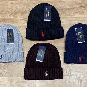 May include: Four cable-knit beanies in grey, black, navy, and brown. Each hat has a folded brim and a small polo player logo. Each beanie has a tag that says "POLO RALPH LAUREN".