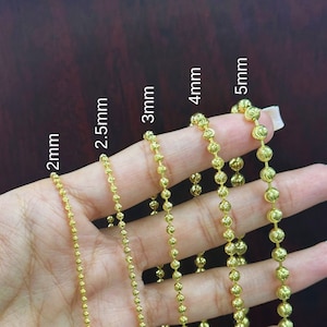 Puede incluir: Seis cadenas de oro de diferentes tamaños, 2 mm, 2,5 mm, 3 mm, 4 mm y 5 mm, se muestran en una mano. Las cadenas están hechas de pequeñas cuentas redondas.