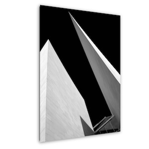 May include: A black and white architectural photograph featuring two sharp, angular building structures reaching towards the sky. The surfaces are composed of light-coloured stone blocks, creating a stark contrast against the deep black background.