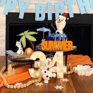 May include: A birthday display featuring a light blue banner reading HAPPY BIRTHDAY, blue balloons, and Olaf figures. The centerpiece includes a wooden sign reading HAPPY BIRTHDAY IN SUMMER, a light-up number 34, a palm tree, and orange fabric.