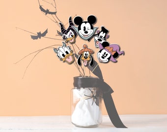 Könnte beinhalten: Ein Glasgefäß mit einem schwarzen Band und einem weißen Stoffbeutel im Inneren. Das Gefäß ist mit einem Spinnennetz verziert und enthält mehrere Halloween-Figurenausschnitte, darunter Mickey Mouse, Donald Duck, Goofy und Pluto.