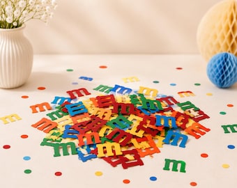 May include: A collection of small, die-cut lowercase letter m shapes in various colors including red, blue, green, and yellow. These paper cutouts are scattered across a surface, accompanied by small, multicolored circular confetti pieces.
