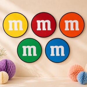 May include: Five circular wall decorations featuring the letter m in white, each with a distinct background colour of yellow, red, orange, green, or blue. Each circle is outlined in black, creating a set of vibrant, uniform, and graphic wall art pieces.