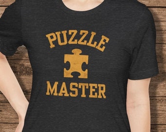 May include: A dark grey t-shirt with the text "PUZZLE MASTER" in yellow, with a yellow puzzle piece graphic in between the words.