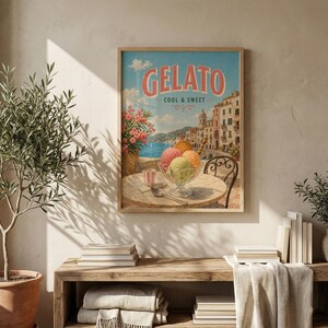 May include: A framed vintage-style print featuring the word "Gelato" in coral lettering. The image depicts a seaside scene with colorful buildings, a table with ice cream, and a glass of water. The sky is blue with fluffy clouds.