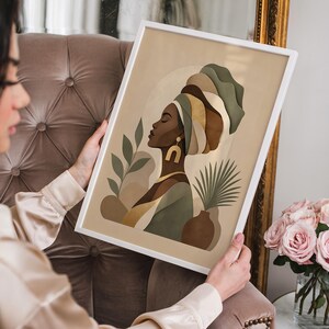 May include: A framed art print featuring a profile of a woman wearing a turban. The artwork uses a palette of beige, brown, and green tones. The woman is adorned with gold jewelry, and the background includes botanical elements.