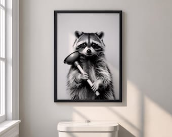 May include: Black and white framed print featuring a raccoon holding a plunger. The raccoon has a bandit mask and fluffy fur. The print is displayed above a white toilet in a bathroom setting.