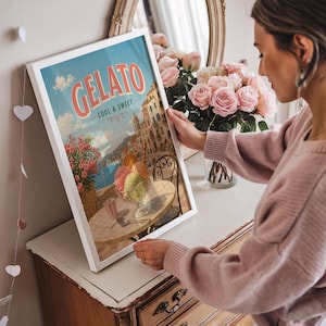 May include: A framed print featuring a vintage gelato advertisement. The artwork displays a coastal Italian scene with gelato in a glass, a table, and the word "Gelato" in a retro font. The print is in a white frame.