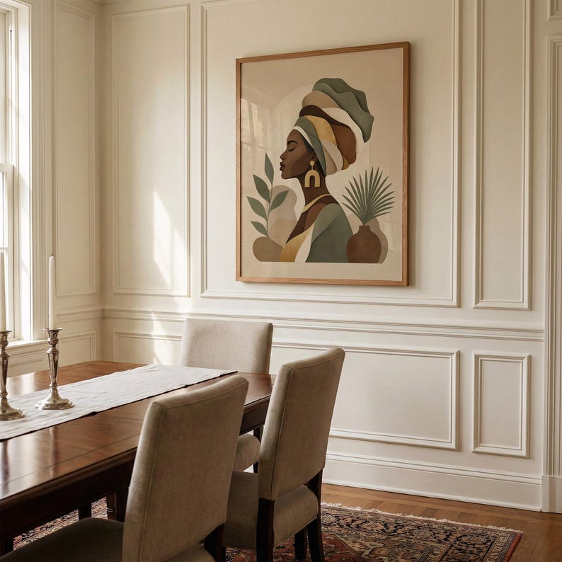 May include: A framed art print featuring a profile of a person wearing a head wrap in shades of green, brown, and yellow. The artwork includes botanical elements and is displayed in a dining room setting with a wooden table and chairs.