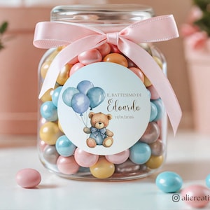 Può includere: Un barattolo di vetro pieno di caramelle colorate, legato con un nastro rosa. Un adesivo rotondo sul barattolo presenta un orsetto con palloncini e il testo "IL BATTESIMO DI Edoardo 11/04/2026".