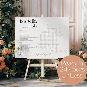Könnte beinhalten: Ein weißes Kreuzworträtselschild auf einer hölzernen Staffelei mit den Namen "Isabella and Josh" oben. Das Rätsel enthält Hinweise auf das Paar. Ein pfirsichfarbener Kreis mit dem Text "Ready In 24 Hours Or Less" befindet sich unten rechts.