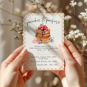 May include: A baby shower invitation with a stack of pancakes topped with berries and syrup. The text "pancakes & pacifiers" is at the top. The invitation includes details for a baby shower brunch honoring "mom-to-be" Keira.