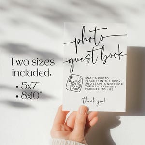 May include: A white photo guest book sign with black script. The sign includes the text "photo guest book", "Two sizes included: 5x7", and "8x10". It also features a camera graphic and the words "Snap a photo, place it in the book, and leave a note for the new baby and parents - to be. Thank you!"