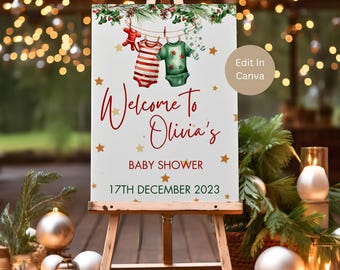 May include: A white welcome sign with a Christmas theme for a baby shower. The sign has a red and green garland with a clothesline of baby clothes hanging from it. The text on the sign reads "Welcome to Olivia's Baby Shower 17th December 2023".