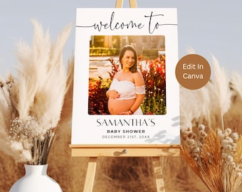 May include: White welcome sign with black text that reads "Welcome to Samantha's Baby Shower December 21st, 20XX". A photo of a pregnant woman in a white dress is in the center of the sign. The sign is on a wooden easel.
