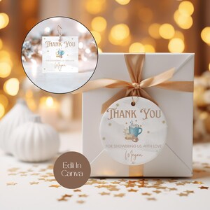 May include: White gift box with a gold ribbon and a round, white thank you tag with a blue and white illustration of a mug of hot chocolate with marshmallows and the text "Thank You" and "For showering us with love Megan".
