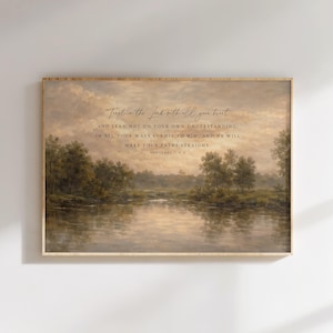 May include: A framed landscape art print featuring a serene river scene with trees and a cloudy sky. The artwork includes the text "Trust in the Lord with all your heart" and other scriptural verses. The frame is a light brown color.