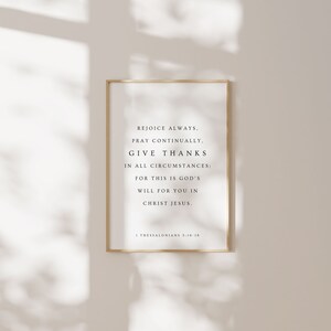 May include: A framed print with a white background and black text. The text reads "Rejoice always, pray continually, give thanks in all circumstances; for this is God's will for you in Christ Jesus." The bottom of the print reads "1 Thessalonians 5:16-18".