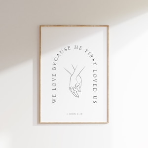 May include: Black and white line art print of two hands holding each other with the text "We love because he first loved us" and "1 John 4:19" below.