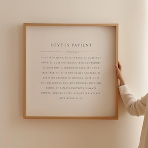 Puede incluir: Una impresión enmarcada con fondo blanco y texto negro. El texto dice "El amor es paciente" e incluye una cita de 1 Corintios 13:4-8. La cita describe las características del amor.