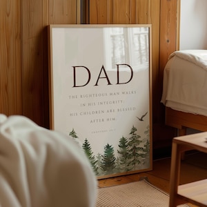 May include: A framed vertical wall art print featuring the word DAD in large dark brown letters at the top. Below the text is the quote: THE RIGHTEOUS MAN WALKS IN HIS INTEGRITY: HIS CHILDREN ARE BLESSED AFTER HIM. PROVERBS 20:7. A watercolor forest scene is at the bottom.