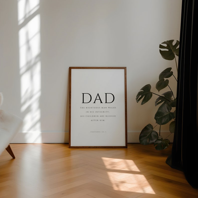 Puede incluir: Una impresi&oacute;n enmarcada con un marco de madera marr&oacute;n. La impresi&oacute;n es blanca con texto negro que dice "DAD" y una cita de Proverbios 20:7: "El hombre justo anda en su integridad: Sus hijos son bendecidos despu&eacute;s de &eacute;l."