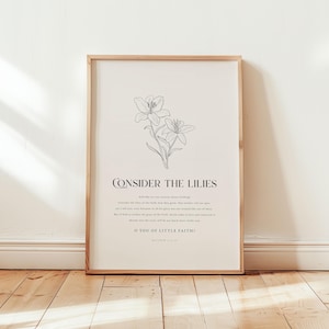 May include: A framed print featuring a line drawing of lilies. The text "CONSIDER THE LILIES" is above a passage from Matthew 6:28-30. The frame is a light wood color, and the background is a cream color.