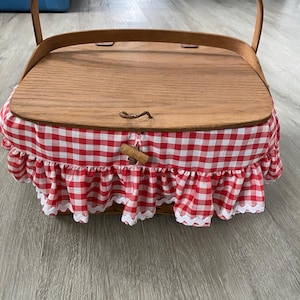 May include: A wooden picnic basket with a red and white gingham fabric lining and a wooden lid. The basket has a handle and a latch.
