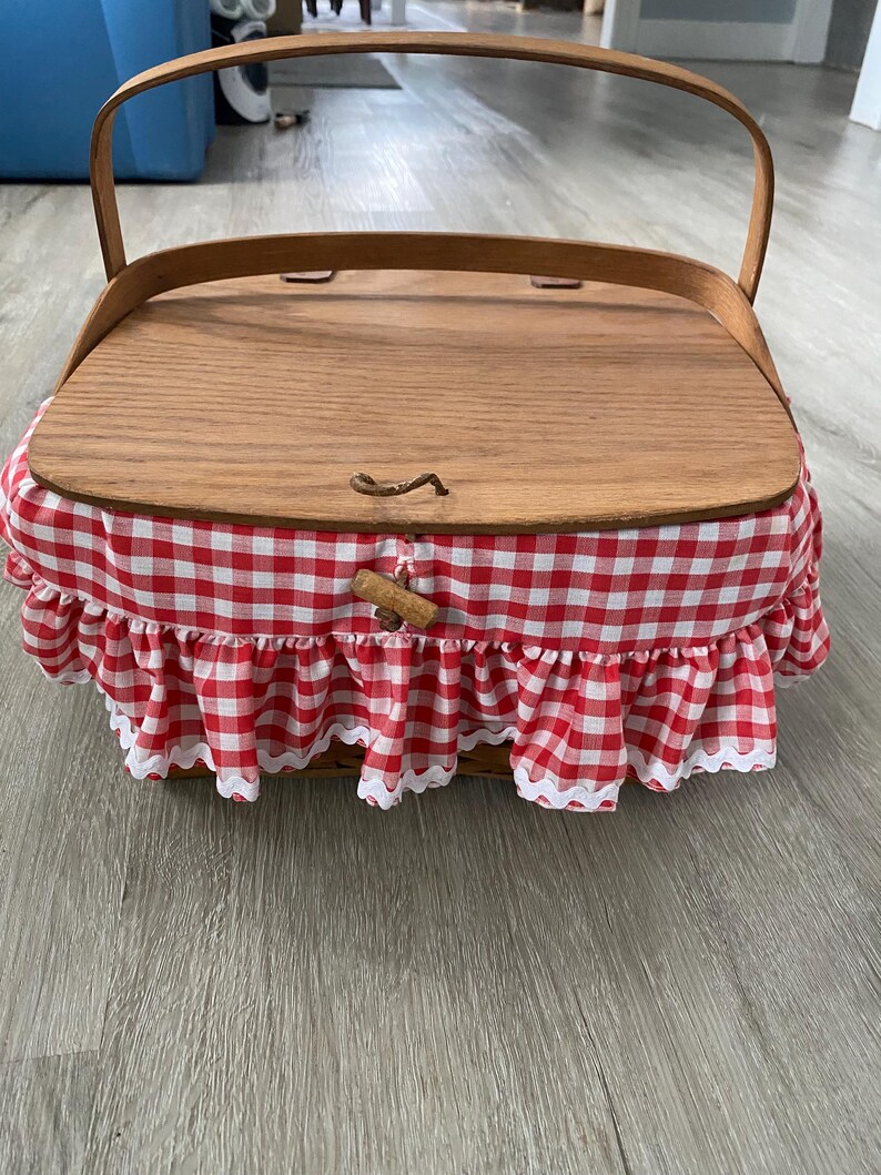 May include: A wooden picnic basket with a red and white gingham fabric lining and a wooden lid. The basket has a handle and a latch.