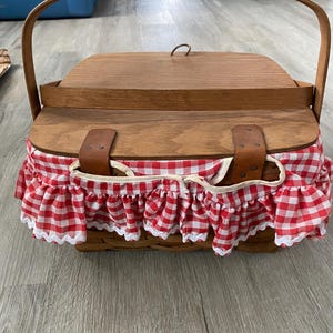 May include: A wooden picnic basket with a red and white gingham fabric lining and a brown leather handle.
