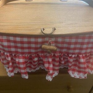 May include: A wooden picnic basket with a red and white gingham lining and a white lace trim. The basket has a wooden handle and a metal clasp.
