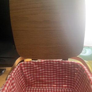 May include: A wooden picnic basket with a red and white gingham lining. The lid is open and the basket is empty.